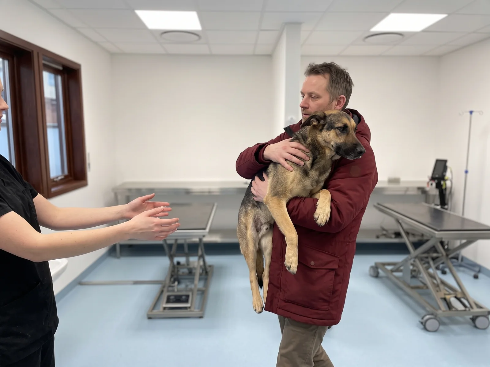 Hundeeier bærer hunden sin inn på klinikken i begge armer mens en dyrepleier strekker hendene fram for å ta imot